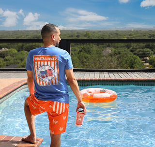 view man standing at pool looking out into the distance. Wearing whataburger american flag table tent t-shirt, orange flying w swim trunks.
