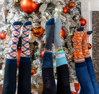 view holiday sock trio in front of christmas tree, argyle navy, day and night, and holiday zig zag.