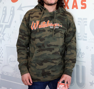 View man wearing a whataburger camo hoodie leaning against a wall.